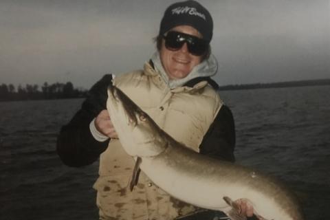 Lady angler with lake in background holding her walleye fish