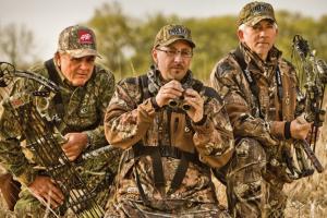 3 Bow Hunters dressed in camo standing together with binoculars scouting prey