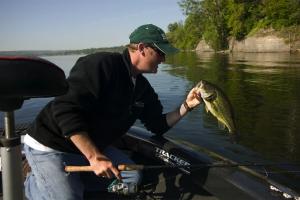 Angler with spinning rod and reel leaning over boat lifing up a largemouth bass